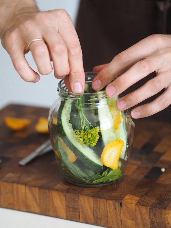 Close-up of hands making pickles with fresh vegetables in a kitchen setting.